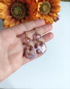 a hand holding two small pink and white glass drop earrings on it's fingers