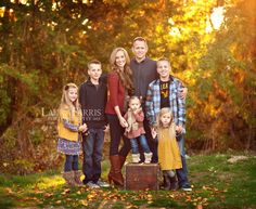 a family poses for a photo in the fall sun with their children and dog on an old suitcase