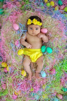 a baby wearing a yellow bow laying on top of an easter basket filled with eggs