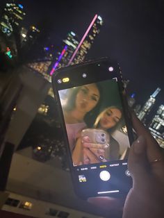 a person holding up a cell phone to take a photo with the city lights in the background