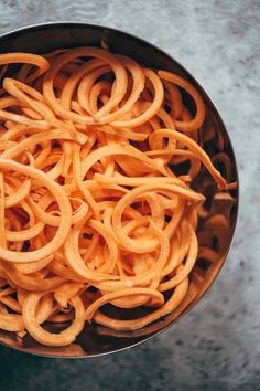 a metal bowl filled with lots of cooked pasta noodles on top of a countertop