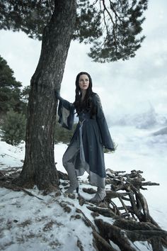 a woman standing next to a tree in the snow