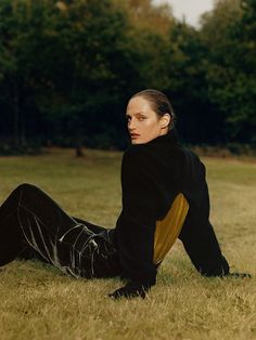 a woman sitting in the grass with her legs crossed and looking off to the side