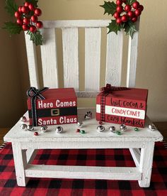 two wooden signs sitting on top of a white bench next to holly wreaths and christmas decorations