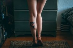 a woman's legs with tattoos on them standing in front of a dresser and rug