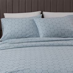 a bed with blue and white comforters on top of it, next to a brown headboard