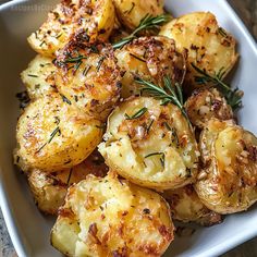 roasted potatoes with herbs and seasoning in a white dish on a wooden table top