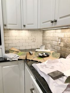 a kitchen with white cabinets and black counter tops covered in paper towels, scissors and other items