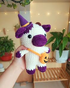 a hand holding a small stuffed animal with a pumpkin in it's mouth and wearing a witches hat