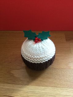 a knitted cupcake with holly on top sitting on a wooden floor next to a red wall