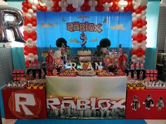 a table topped with lots of candy and balloons in front of a sign that says roblox