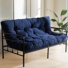 a blue futon sofa sitting on top of a hard wood floor next to a potted plant