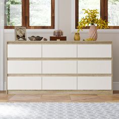 a white dresser sitting in the middle of a living room next to two large windows