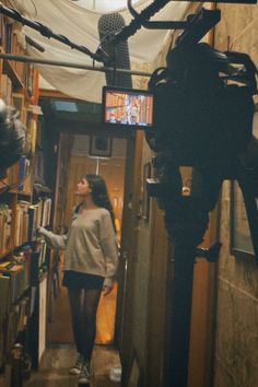 a woman walking down a hallway in front of a microphone and bookshelf filled with books