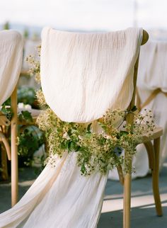 the back of a chair covered in flowers and greenery with white drapes draped over it