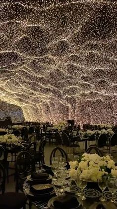 a large room with tables and chairs under a ceiling covered in white flowers on top of it