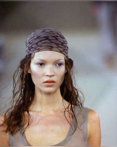 a woman with long hair wearing a gray top and head scarf on the catwalk