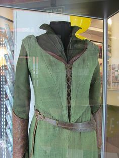 a green dress with brown leather trims and a yellow helmet on display in a glass case