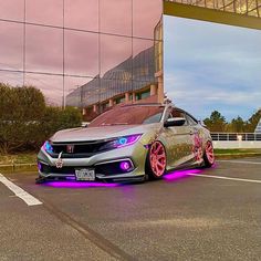 a silver car with pink rims parked in a parking lot next to a building