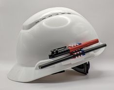 a white hard hat with tools attached to the side and two screwdrivers on top