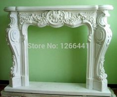 a white marble fireplace mantel with carvings on the top and sides, in front of a green wall