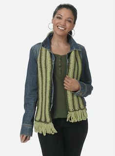 a woman wearing a jean jacket and green sweater smiles at the camera while standing in front of a white background