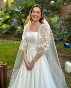 a woman wearing a wedding dress and veil posing for a photo in front of some trees