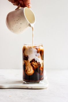 a person pouring coffee into a glass with liquid in it on a white table top