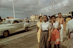 an old photo of some people on a boardwalk with cars and buildings in the background