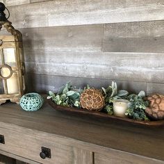 a wooden table topped with a tray filled with succulents and an old lantern