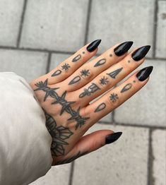 a woman's hand with black nail polish and tattoos on it