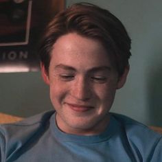 a young man is smiling and looking at his cell phone while sitting on the couch