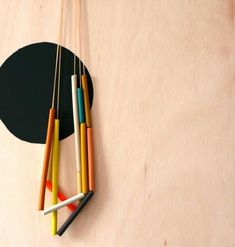 several colored pencils are hanging on a wooden wall with a black circle in the background