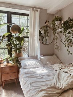 an unmade bed in a bedroom with plants hanging on the wall and a round mirror above it