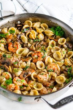 a skillet filled with pasta and shrimp on top of a white table cloth next to utensils