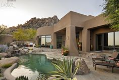 a house with a pool in front of it and some rocks around the back yard