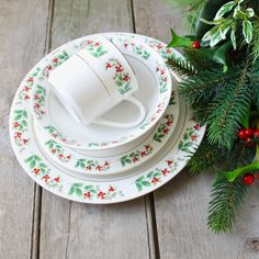 a stack of white dishes sitting on top of a wooden table next to christmas greenery