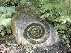 a rock with a spiral painted on it in the grass next to some trees and bushes