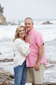 a man and woman standing next to each other near the ocean with waves crashing on them