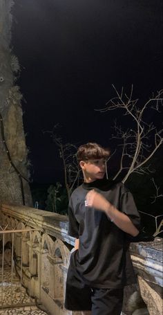 a boy is standing on a bridge at night with his hand in his pocket and looking off into the distance