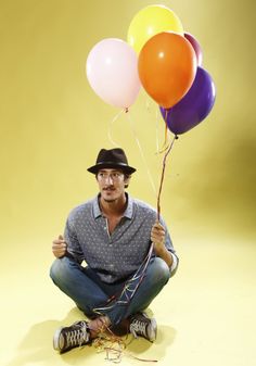 a man in a hat and glasses holding several balloons with string attached to his legs