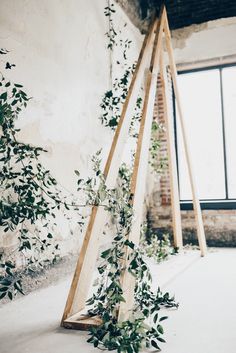 an art installation made out of wood and greenery in front of a large window