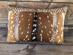 an animal print pillow sitting on top of a wooden bench next to a brick wall