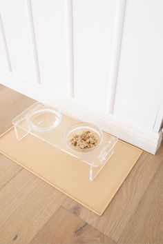 a cat eating food out of a plastic bowl on the floor next to a door