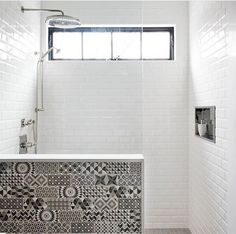 a white tiled bathroom with black and white tiles on the shower wall, tub, and window