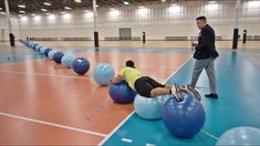 two men are doing exercises on exercise balls in an indoor gym while one man watches