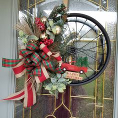 a bicycle wheel decorated with greenery and ribbons on the front door to give it a festive touch