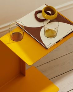 a pair of glasses sitting on top of a yellow table next to a book and cup