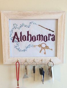 there is a cross stitch frame with keys hanging from it and the word alohora written in cursive letters