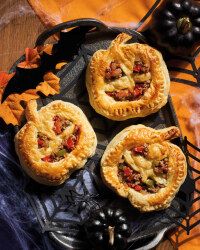 four small pies sitting on top of a black plate next to grapes and pumpkins